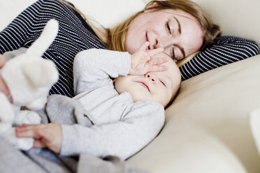 Tired baby girl and mother reclining on sofa - CUF21712