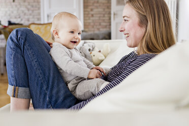 Baby girl and mother face to face on sofa - CUF21713