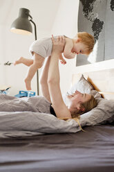 Mid adult woman holding up baby daughter in bed - CUF21722