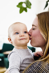 Frau trägt ihre kleine Tochter und küsst sie auf die Wange - CUF21743