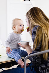 Mid erwachsene Frau füttert Baby Tochter auf dem Küchentisch - CUF21744