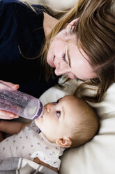 Overhead view of mid adult woman feeding bottle to baby daughter on sofa - CUF21750