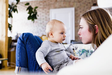 Mid adult woman and baby daughter pulling faces on sofa - CUF21754