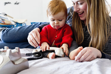 Baby-Mädchen und Mutter auf dem Bett spielen mit Festnetztelefon - CUF21756