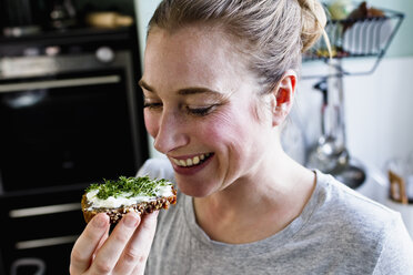 Mittlere erwachsene Frau isst Roggenbrot-Snack in der Küche - CUF21761