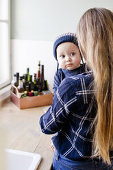 Woman carrying baby son wearing knit hat in kitchen - CUF21763