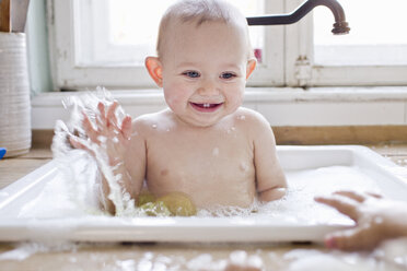 Baby boy splashing whilst bathing in kitchen sink - CUF21766