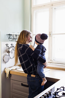 Mittlere erwachsene Frau trägt ihren kleinen Sohn in der Küche - CUF21769