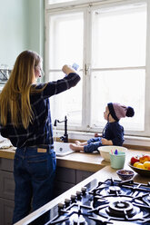 Mid adult woman pouring water into kitchen sink for baby son - CUF21770