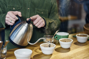 Mann gießt kochendes Wasser in Kaffeeschalen zur Verkostung auf der Kaffeetheke - CUF21790