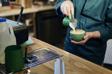 Abgeschnittene Aufnahme eines männlichen Barista, der Milch in eine Kaffeetasse in einem Coffeeshop gießt - CUF21798