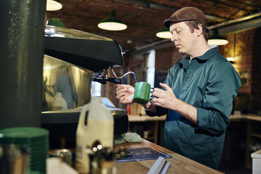 Männlicher Barista erhitzt Milchkännchen an der Kaffeemaschine in einem Coffeeshop - CUF21799