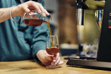 Hände eines männlichen Barista, der kalt gebrühten Kaffee in ein Weinglas auf dem Tresen eines Cafés gießt - CUF21805