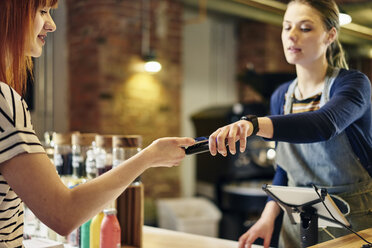 Female barista taking smartphone contactless payment from coffee shop customer - CUF21806