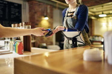 Female barista taking smartphone contactless payment from coffee shop customer - CUF21807