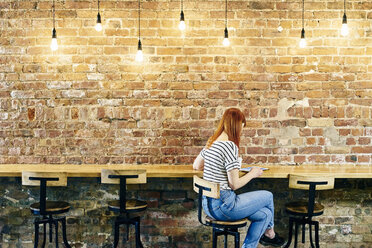 Female customer sitting at brick wall bench browsing digital tablet in coffee shop - CUF21810