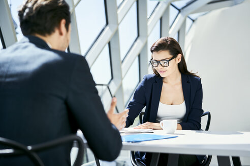 Businesswoman and businessman talking at desk in modern office - BSZF00456