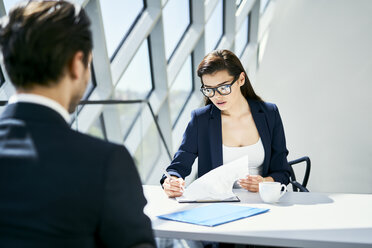 Businesswoman with businessman at desk checking documents in modern office - BSZF00459