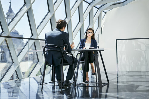 Businesswoman and businessman talking at desk in modern office - BSZF00461