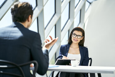 Businesswoman and businessman talking at desk in modern office - BSZF00463