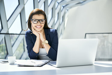 Porträt einer lächelnden Geschäftsfrau, die in einem modernen Büro am Schreibtisch sitzt - BSZF00472