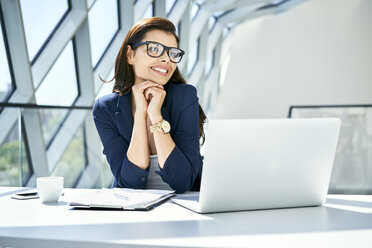 Lächelnde Geschäftsfrau sitzt am Schreibtisch in einem modernen Büro - BSZF00473