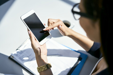 Nahaufnahme einer Geschäftsfrau, die ein Mobiltelefon am Schreibtisch im Büro benutzt, lizenzfreies Stockfoto