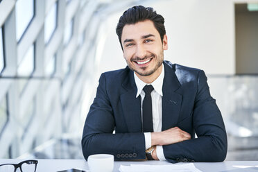 Porträt eines lächelnden Geschäftsmannes am Schreibtisch in einem modernen Büro - BSZF00483
