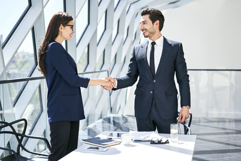 Businesswoman and businessman shaking hands in modern office - BSZF00492