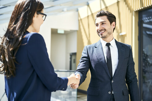 Smiling businessman and businesswoman shaking hands in office - BSZF00493