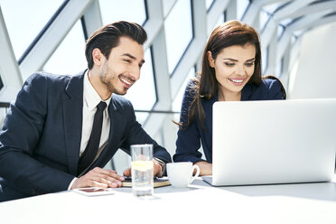 Smiling businesswoman and businessman using laptop at desk in modern office - BSZF00494