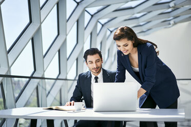 Smiling businesswoman and businessman using laptop at desk in modern office - BSZF00497