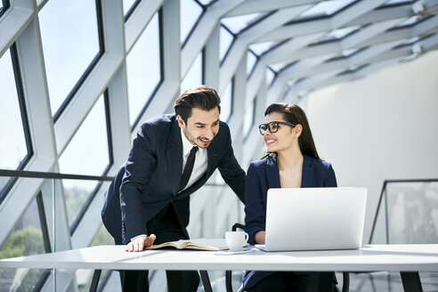 Lächelnde Geschäftsfrau und Geschäftsmann mit Laptop am Schreibtisch in einem modernen Büro - BSZF00498