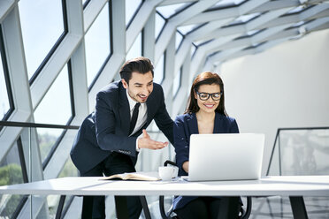 Lächelnde Geschäftsfrau und Geschäftsmann mit Laptop am Schreibtisch in einem modernen Büro - BSZF00499