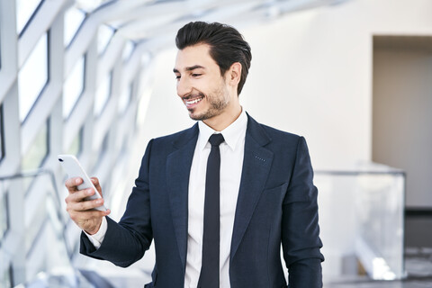 Lächelnder Geschäftsmann schaut auf sein Handy, lizenzfreies Stockfoto