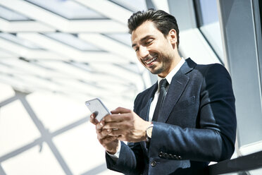 Lächelnder Geschäftsmann schaut auf sein Handy - BSZF00534