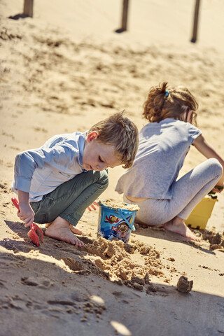 Bruder und Schwester spielen mit Sand am Strand, lizenzfreies Stockfoto