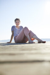Lächelnde Frau sitzt auf einem Steg am See - PNEF00648