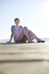 Smiling woman sitting on jetty at lake - PNEF00648