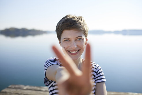 Porträt einer lächelnden Frau vor einem See mit Siegeszeichen - PNEF00649