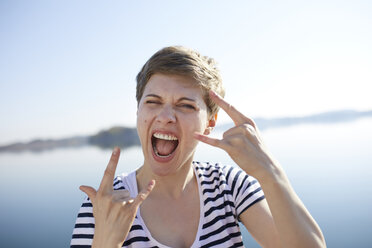 Portrait of screaming woman in front of lake showing Rock And Roll Sign - PNEF00654