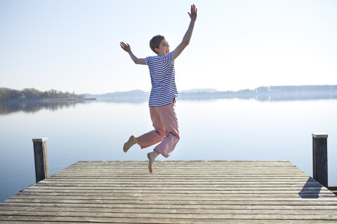 Germany, Bavaria, back view of woman jumping in the air in front of lake stock photo