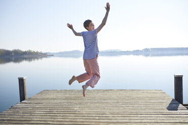 Germany, Bavaria, back view of woman jumping in the air in front of lake - PNEF00656