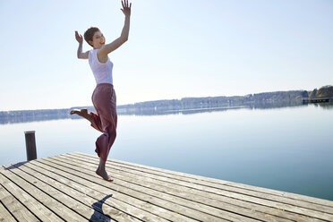 Happy woman jumping in the air on jetty - PNEF00670