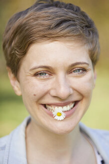 Porträt einer lachenden Frau mit Gänseblümchen im Mund - PNEF00672