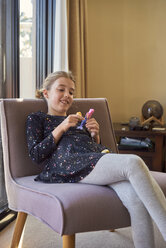 Lächelndes Mädchen, das zu Hause auf einem Sessel sitzt und mit einer Puppe spielt - BEF00138