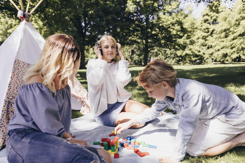 Zwei junge Frauen und ein Junge spielen mit Bauklötzen in einem Park, lizenzfreies Stockfoto