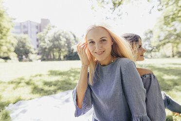 Porträt von zwei lächelnden jungen Frauen, die sich in einem Park entspannen - KMKF00276