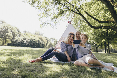 Zwei junge Frauen und ein Junge machen ein Selfie neben einem Tipi in einem Park, lizenzfreies Stockfoto