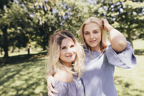 Portrait of two smiling young women embracing in a park - KMKF00285